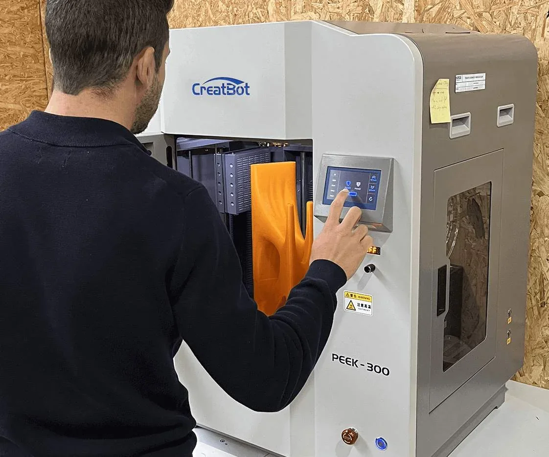 Man operating Creatbot PEEK-300 3D printer, displaying a large orange print, in an industrial setting with visible branding.