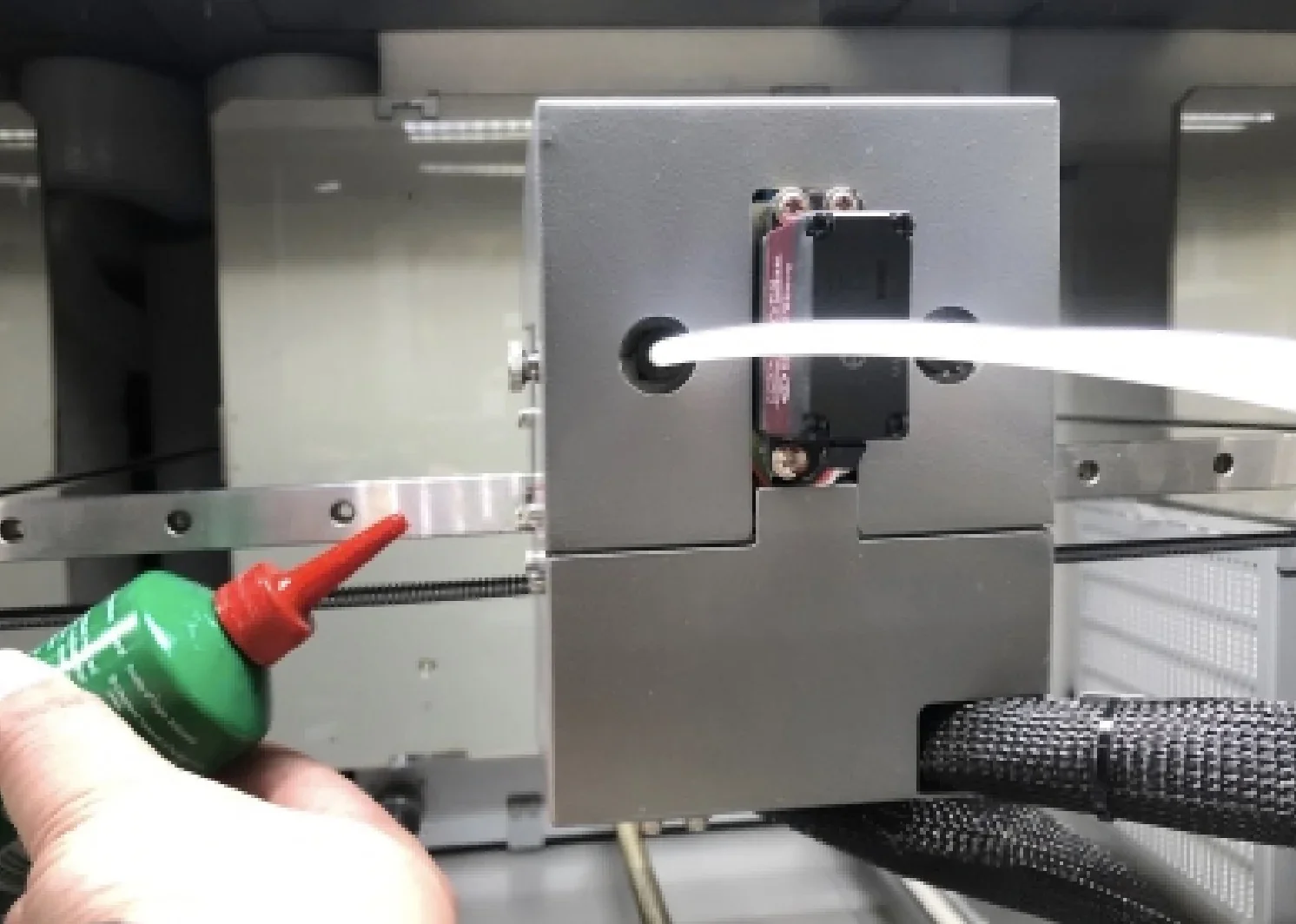 CreatBot PEEK-300 3D printer part in focus with filament tube, hand applying lubricant, showcasing machine's maintenance process in detail.