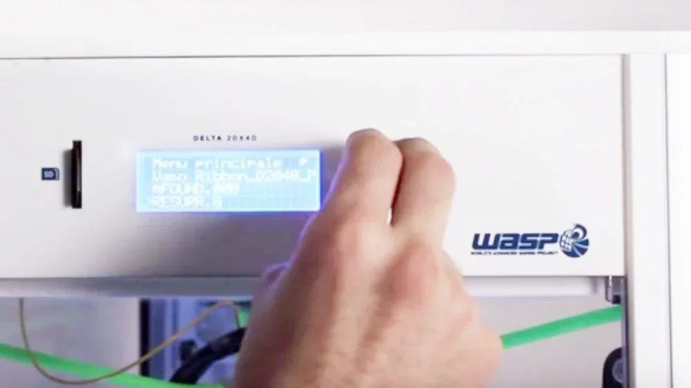 Hand operating control panel on Delta WASP 2040 Clay 3D printer. Screen displays settings. Visible WASP branding.