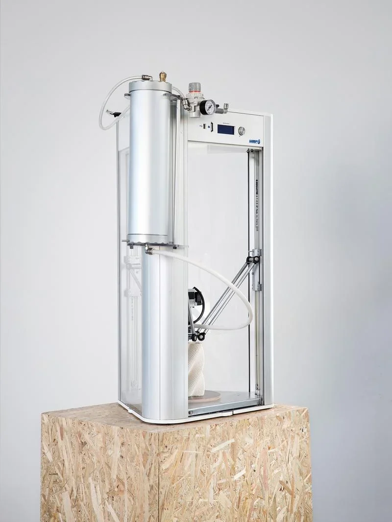 Delta Wasp 2040 Clay 3D printer on a wooden stand, featuring a cylindrical metal tank, designed for clay printing.