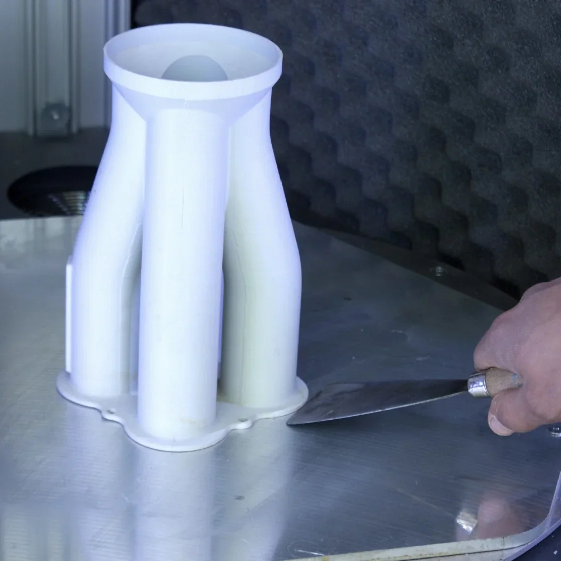 Delta Wasp 2040 Industrial X prints a white multi-tube part, being removed with a spatula in a workshop setting.