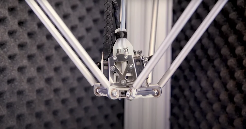 Delta Wasp 2040 Industrial X print head with metal arms in motion, surrounded by soundproof padding in a high-tech industrial setting.
