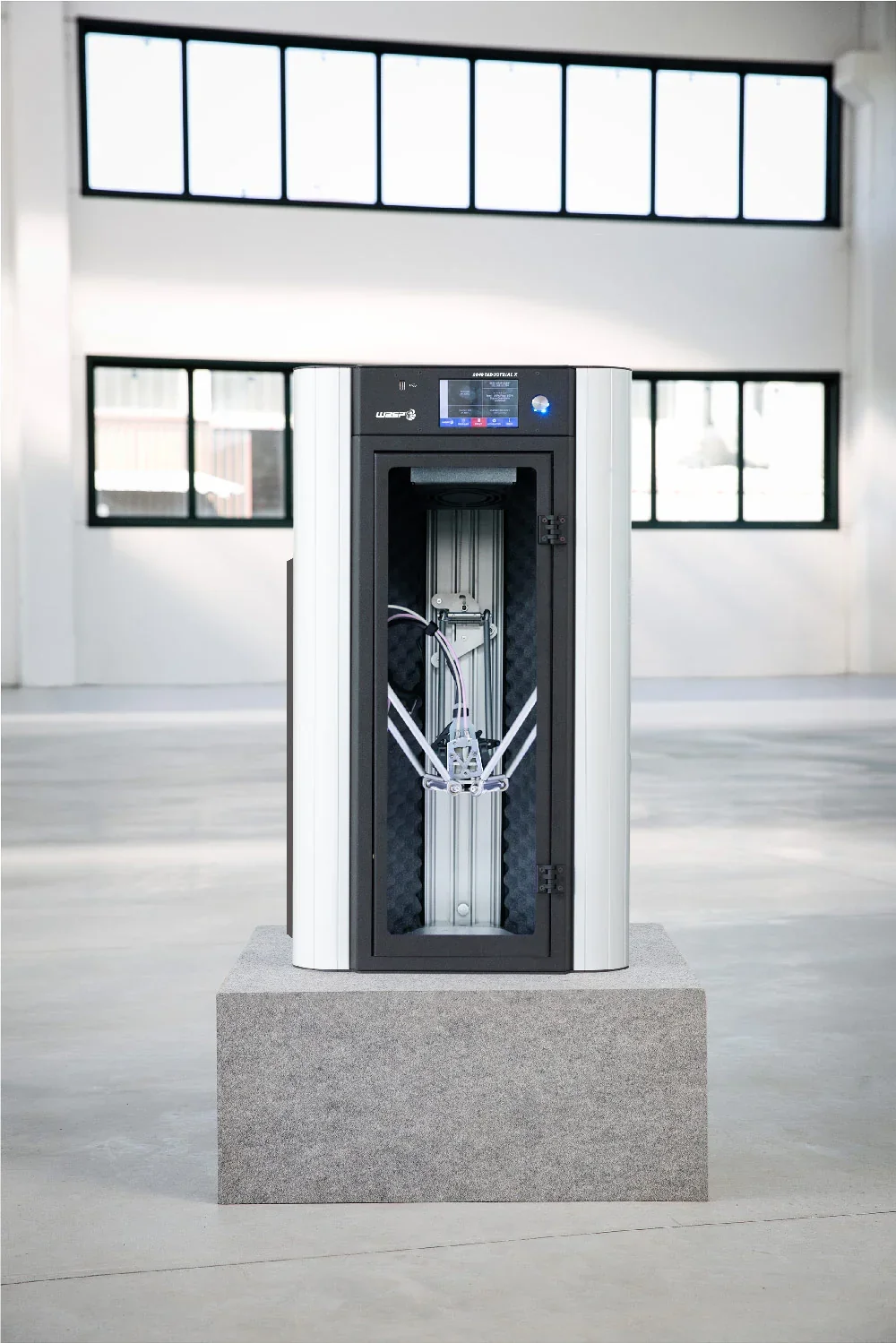 Delta Wasp 2040 Industrial X 3D printer on a stone pedestal in a bright room with large windows, showcasing advanced printing mechanics.