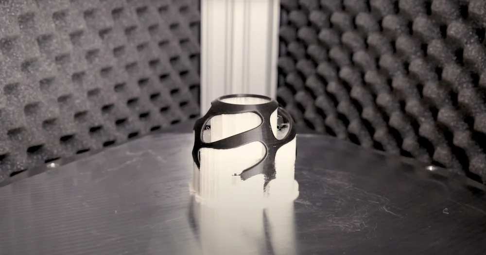 Delta Wasp 2040 Industrial X creates a black and white 3D-printed geometric object on a reflective surface, surrounded by foam panels.