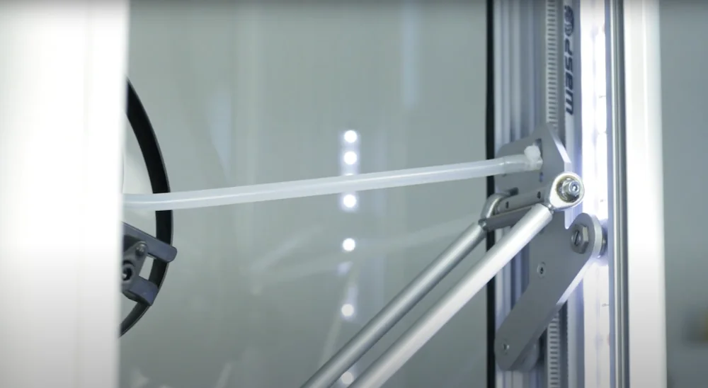 Delta WASP 2040 Pro 3D printer close-up, showing arm mechanism and filament guide tube inside an illuminated enclosure, with visible branding.