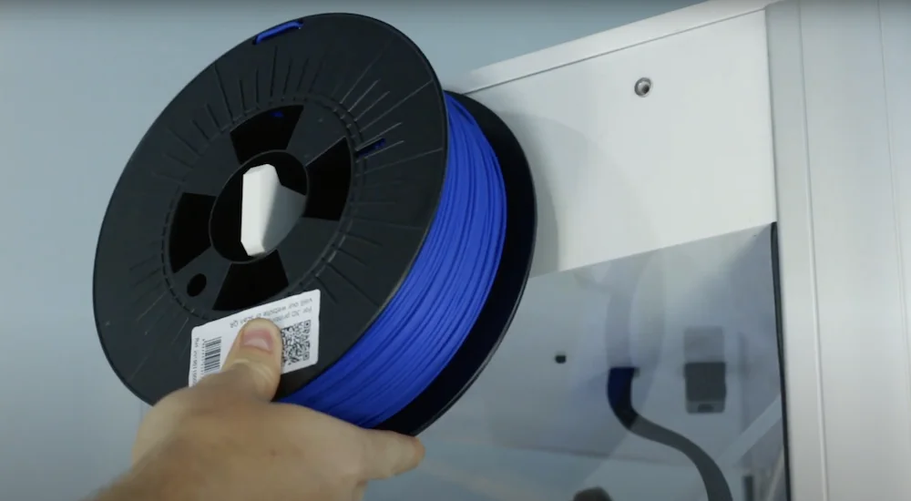 Blue filament spool being installed on a Delta WASP 2040 Pro 3D printer, showing hand positioning the filament for use.