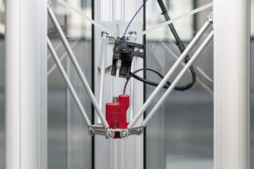 Delta WASP 2040 Pro 3D printer nozzle close-up, featuring mechanical arms and wiring, set within a clear, cylindrical frame for precise printing.