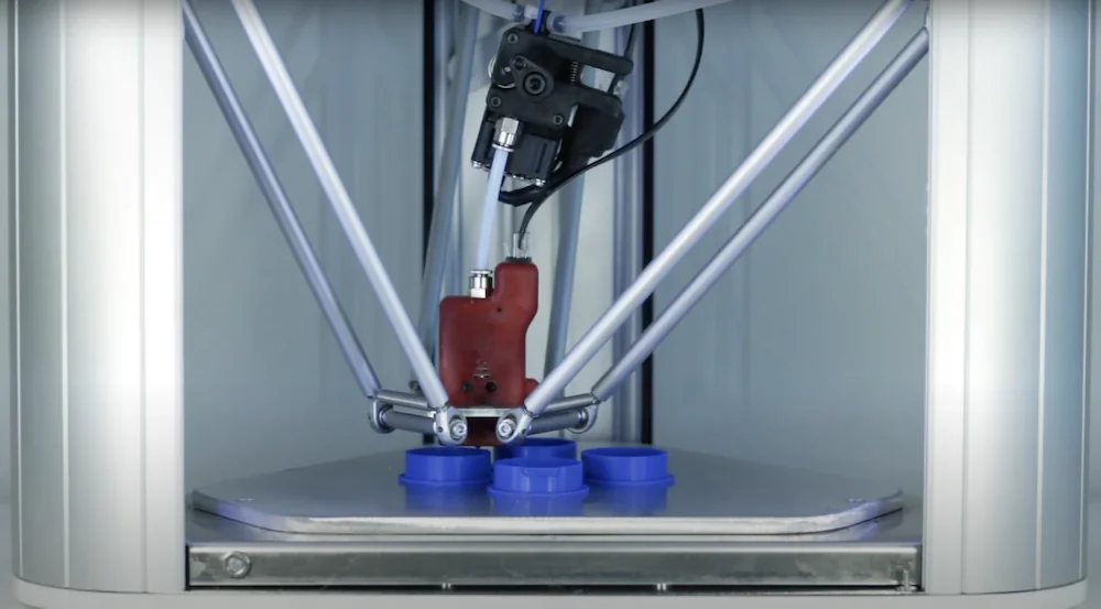 Delta Wasp 2040 Pro 3D printer with robotic arm creating blue circular parts inside a metallic enclosure.