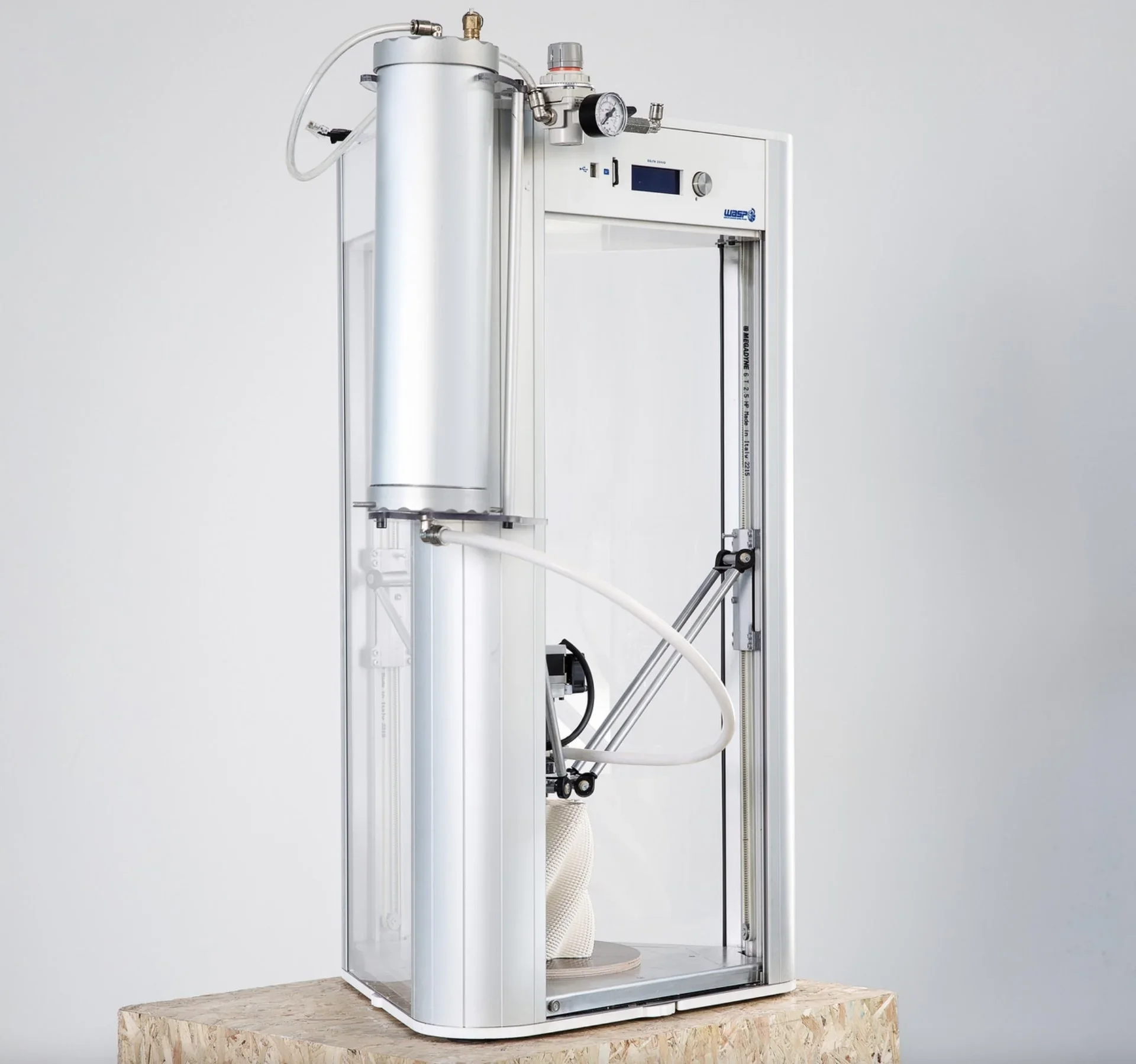 Delta Wasp 2040 Pro 3D printer on a wooden base, displaying a printed white object. Silver cylindrical design with visible tubes and digital control.