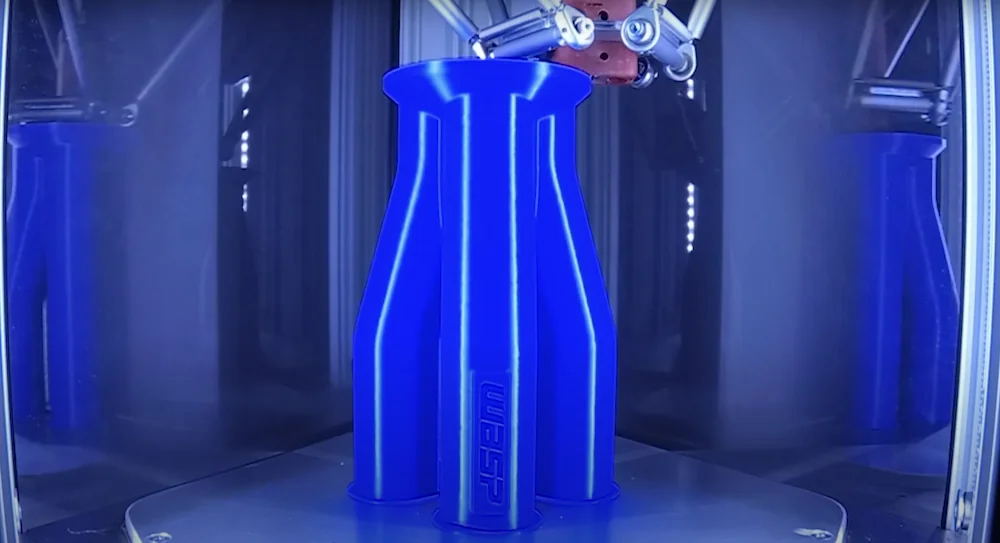 Delta WASP 2040 Pro 3D printer creating a tall, blue geometric vase, branded with "WASP" inside a transparent enclosure.