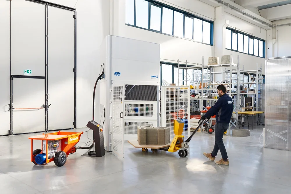 Delta WASP 3MT in a workshop, with a worker handling concrete parts created by the printer, showcasing its industrial 3D printing capabilities.
