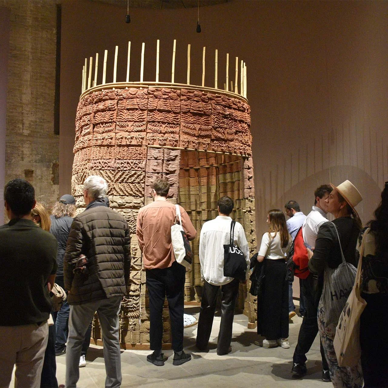 People observing a large, intricately patterned, clay structure printed by Delta Wasp 3MT, displayed in a gallery setting with soft lighting.