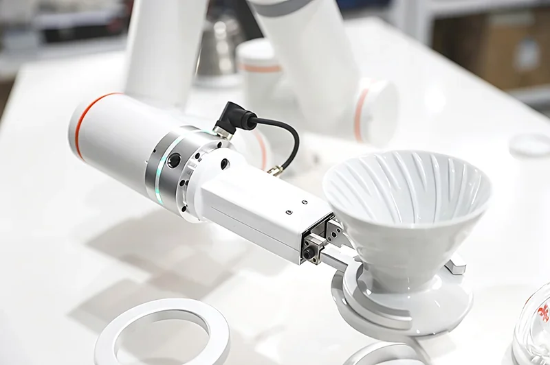 Robotic arm fairino fr3 assembling a coffee dripper on a white table, showcasing its precision in handling small parts.