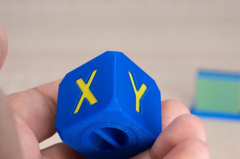 A detailed image shows a 3D printed calibration cube created by a Flashforge printer. The cube is predominantly blue with yellow insets forming the letters 