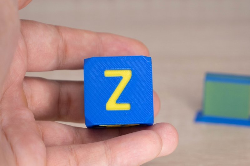 A person holds a 3D-printed blue cube with a yellow letter 