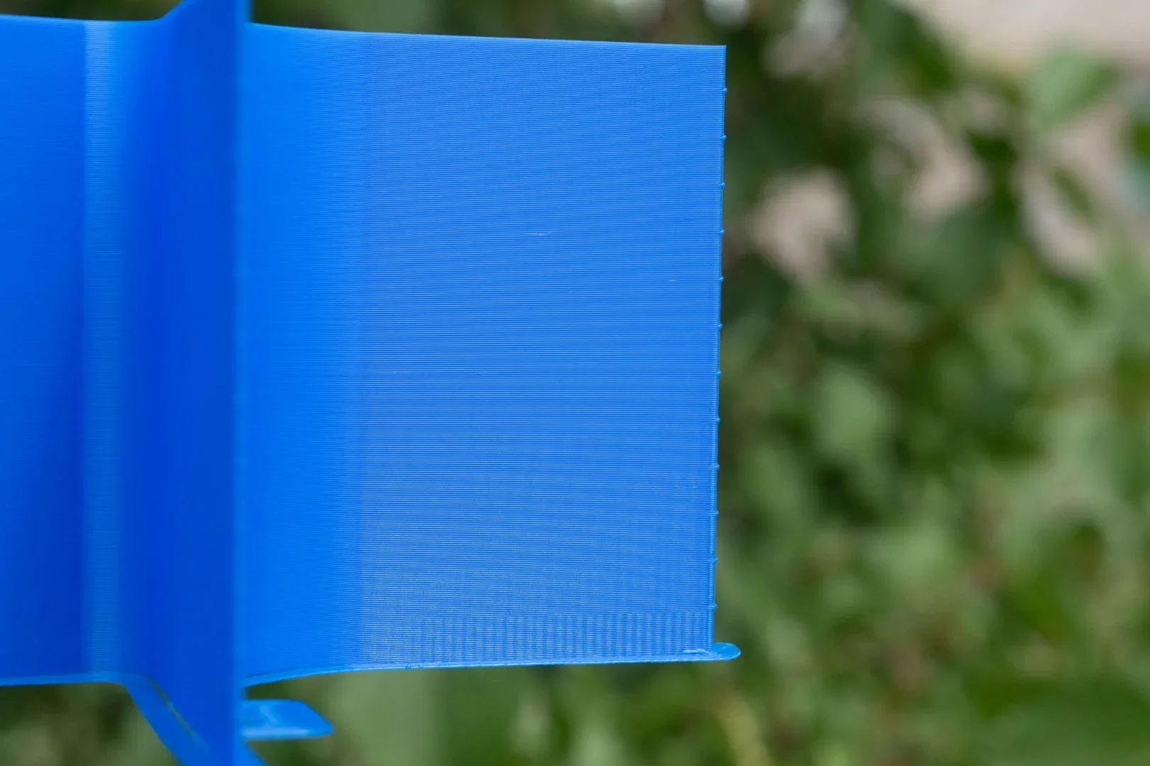 Close-up of a blue 3D printed object with fine horizontal layers created by Flashforge AD5X against a blurred green background.