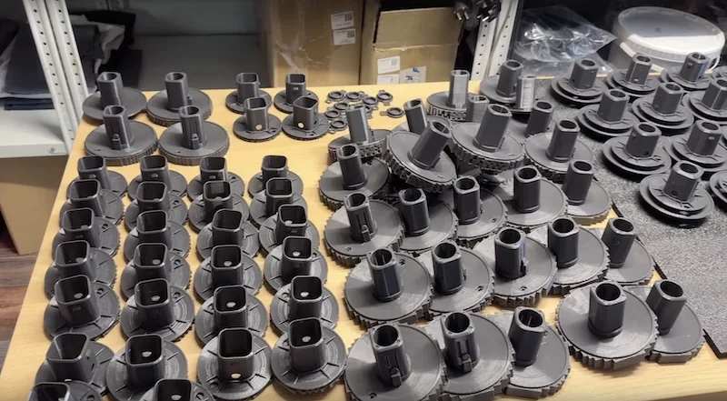 Flashforge AD5X 3D printed parts on a table, displayed in organized rows, with shelves and boxes in the background.