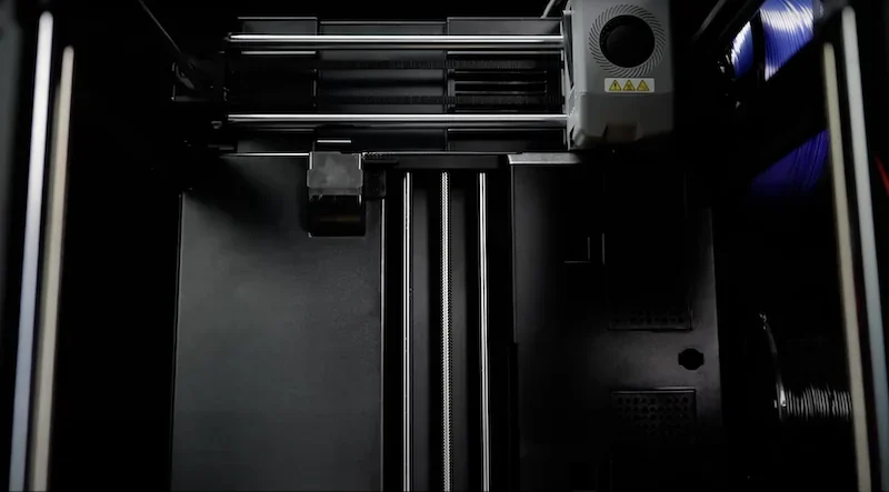 Flashforge AD5X 3D printer interior showing build platform, extruder mechanism, linear rails, and filament spools, highlighting precision printing.