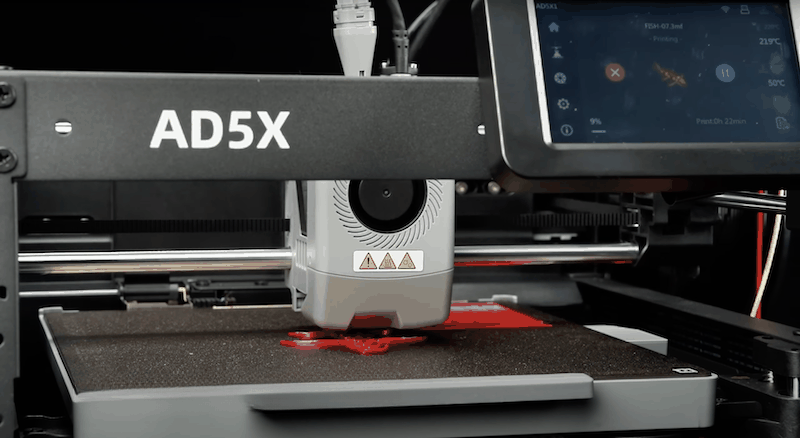 The image showcases the Flashforge AD5X 3D printer. The main body of the printer is visible, featuring a sleek, industrial design with the product name 