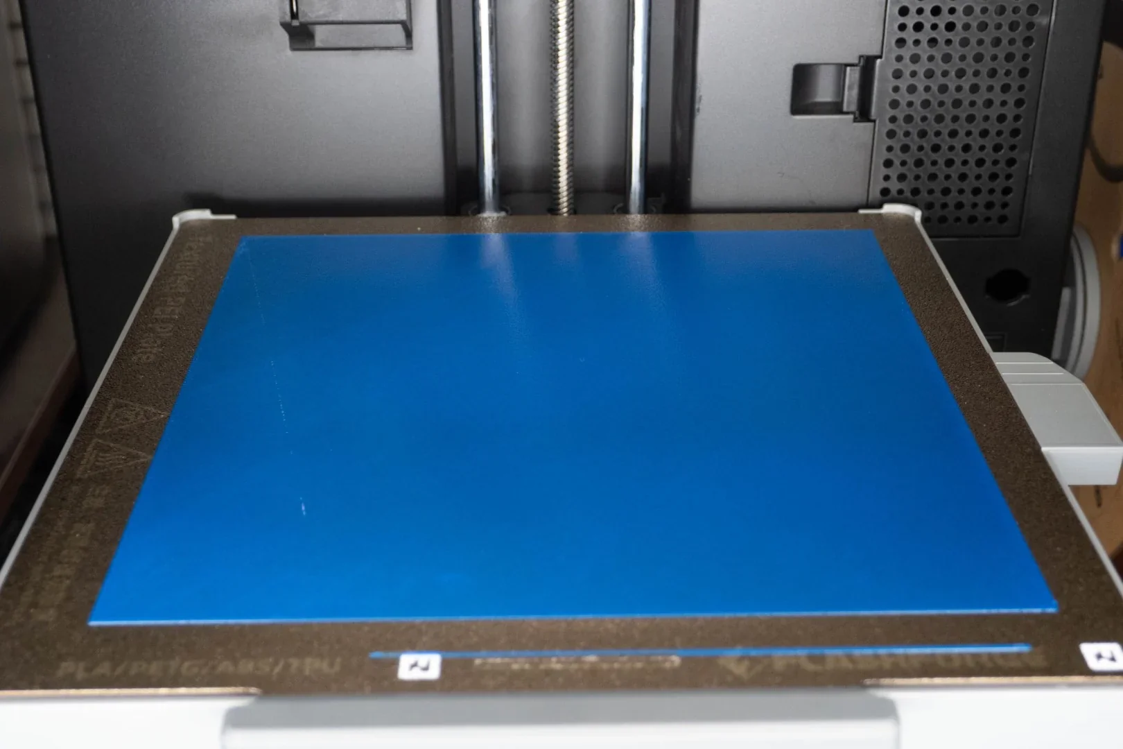 Flashforge AD5X 3D printer with a blue print bed, ready for printing. Brown edges with material labels visible, indicating use for 3D part creation.