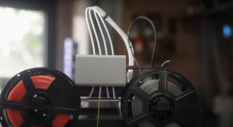 Flashforge AD5X 3D printer side view showing filament reels and connected cables in a workshop setting, highlighting its dual-color printing capability.