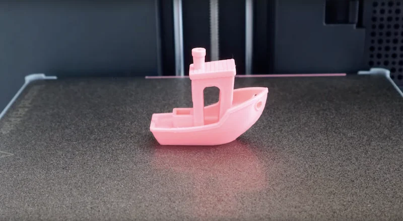 Flashforge AD5X 3D printer with pink boat model on build plate, showcasing precise printing capabilities in a sleek black housing.
