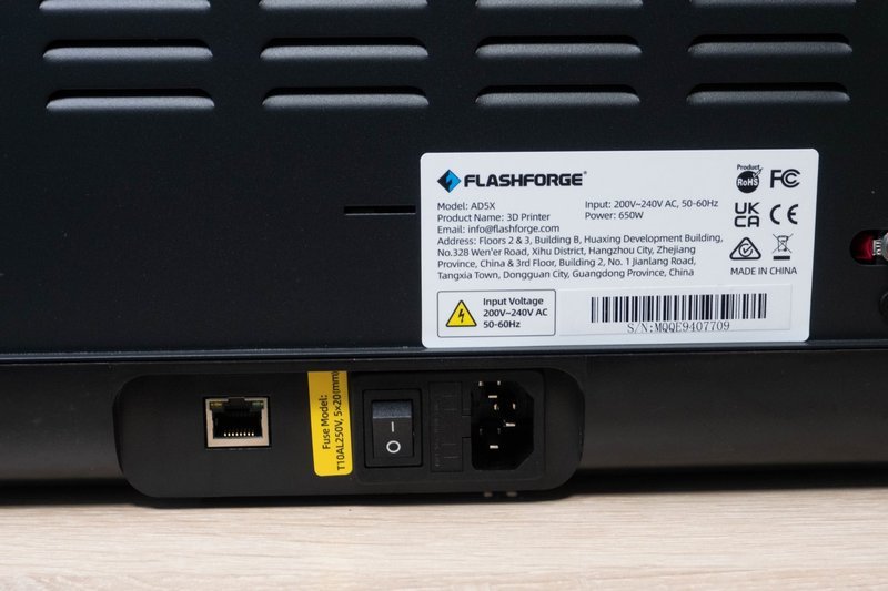 The image shows the back panel of the Flashforge AD5X 3D printer, featuring a black casing with horizontal ventilation slits. A prominent label displays the Flashforge logo, model name 