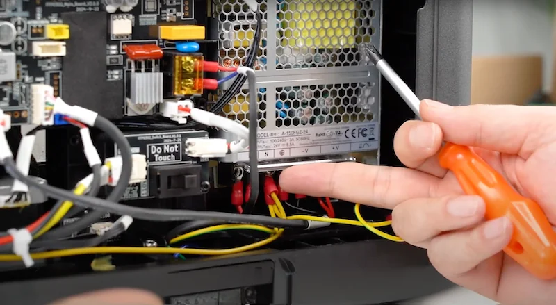 Flashforge AD5X internal components being shown with wiring and circuit board, hand holding screwdriver indicates repair or setup process.