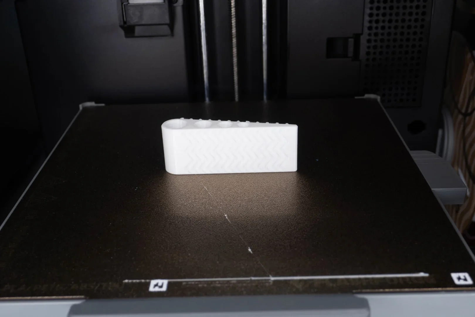 Flashforge Ad5x 3D printer printing a textured white plastic component on its build plate.
