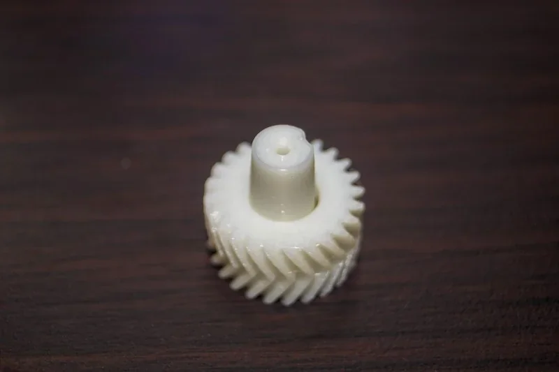 White 3D-printed gear on wood surface, created by FlashForge Adventurer 5M.