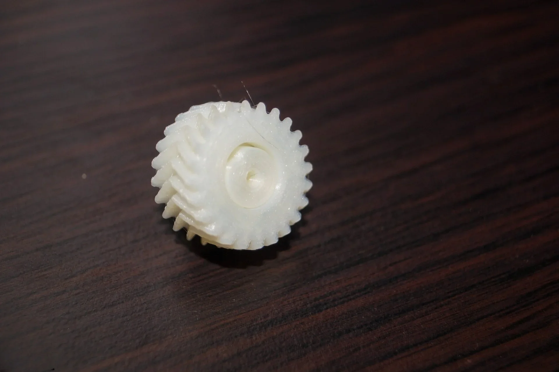 White 3D-printed gear on wooden surface, created by Flashforge Adventurer 5M.