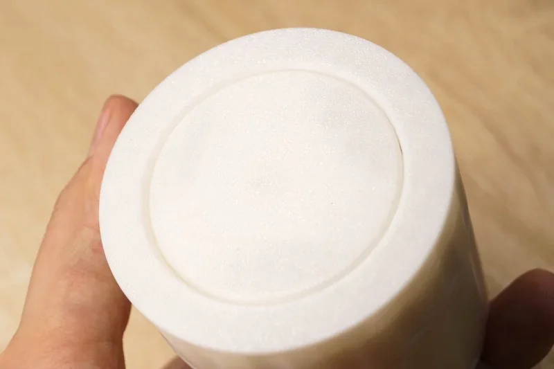 Hand holds a white 3D-printed cylindrical object, crafted by the Flashforge Adventurer 5M, against a wooden surface background.