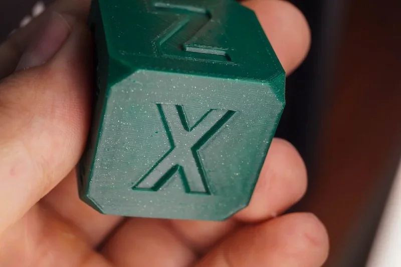 Green 3D-printed cube with "X" and "Z" engravings, created by Flashforge Adventurer 5M, held in hand, showcasing detailed print quality.