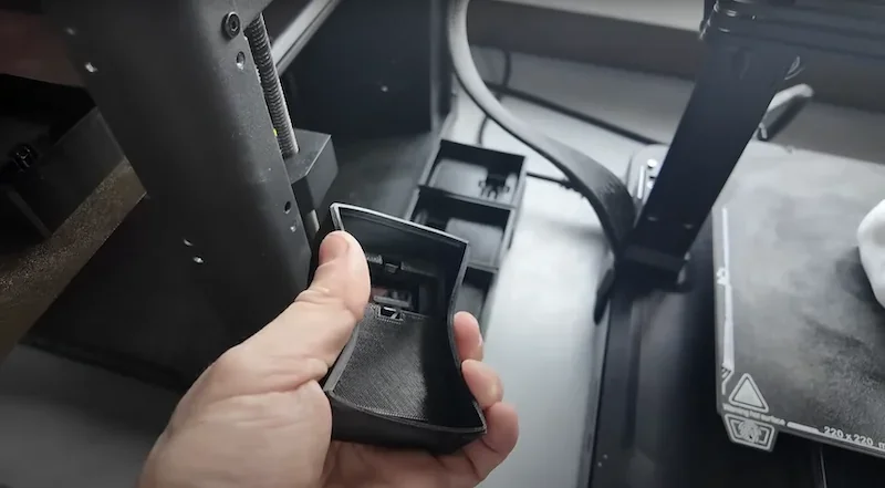 Flashforge Adventurer 5M 3D printer workspace with a hand holding a printed part, showcasing its capabilities and interior components.