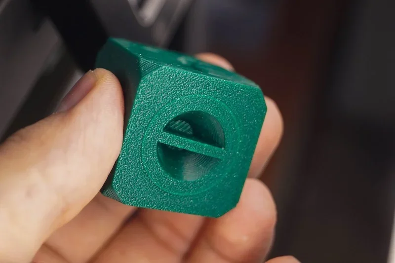 Hand holds green 3D-printed hexagonal part with circular cutout, created by FlashForge Adventurer 5M, showcasing texture and precision.