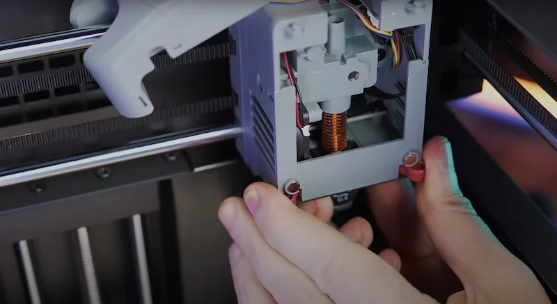 Hands adjust nozzle mechanism of Flashforge Adventurer 5M 3D printer, showing internal components and wiring setup in a detailed, close-up view.