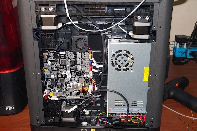 Flashforge Adventurer 5M internal components, including circuit board and power unit, on a desk, showing tech details and setup.