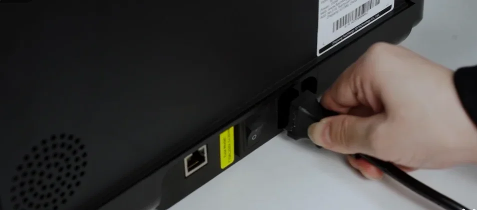 Hand plugging in the power cable into the back of a Flashforge Adventurer 5M 3D printer, near Ethernet and power switch, showcasing connectivity setup.