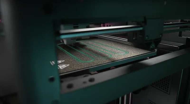 Flashforge Adventurer 5M printing chamber with precision nozzle and print samples on bed, highlighted by ambient lighting.