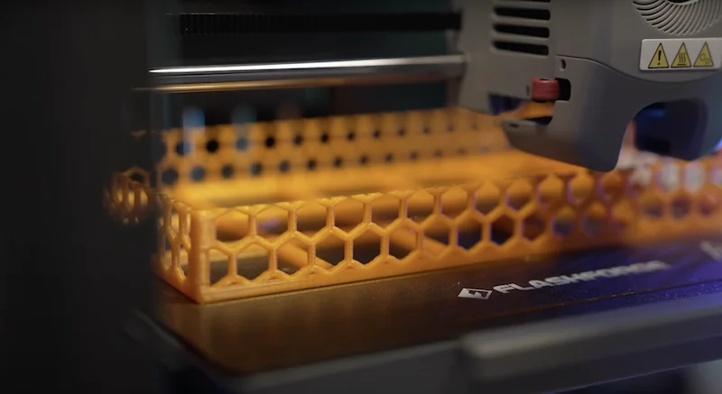 Flashforge Adventurer 5M printing a honeycomb-style structure on a branded platform, showcasing its detailed 3D printing capabilities.