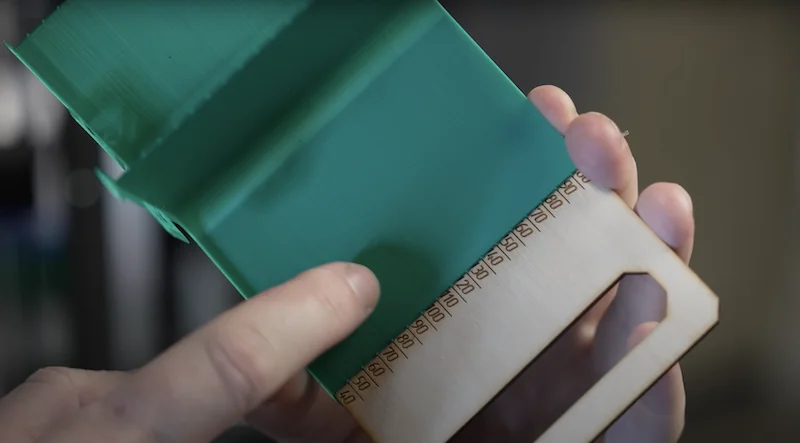 Flashforge Adventurer 5M 3D print sample held by hands, showing green and wood-like materials with detailed textures and engraved numbers.