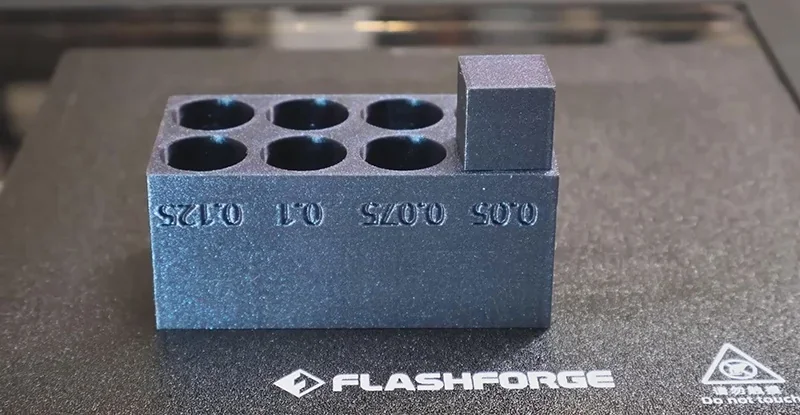 Flashforge Adventurer 5M Pro 3D-printed model with six round slots and raised square block, on branded printer platform.