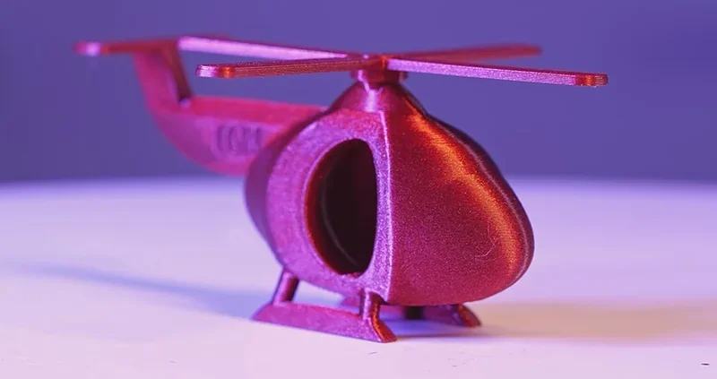 Red 3D-printed helicopter model on a white surface against a purple background, created by Flashforge Adventurer 5M Pro.