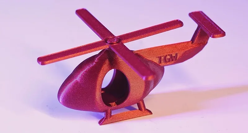 3D-printed red helicopter model by Flashforge Adventurer 5M Pro, showcasing detail and precision, set on a light surface with soft lighting.