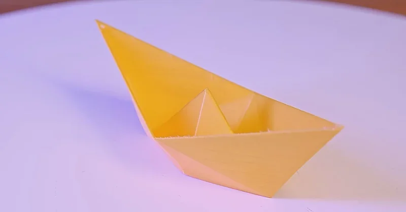 Yellow 3D-printed paper boat model created by Flashforge Adventurer 5M Pro on a white surface, showcasing precision and quality of the print.