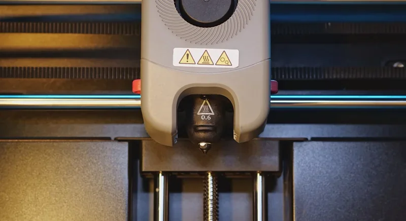 Flashforge Adventurer 5M Pro nozzle close-up with safety warnings, black nozzle marked 0.6, and a visible metal rod in the 3D printing area.