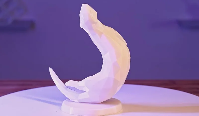 Flashforge Adventurer 5M Pro 3D-printed abstract white sculpture on a table, showcasing intricate facets and curves against a purple backdrop.