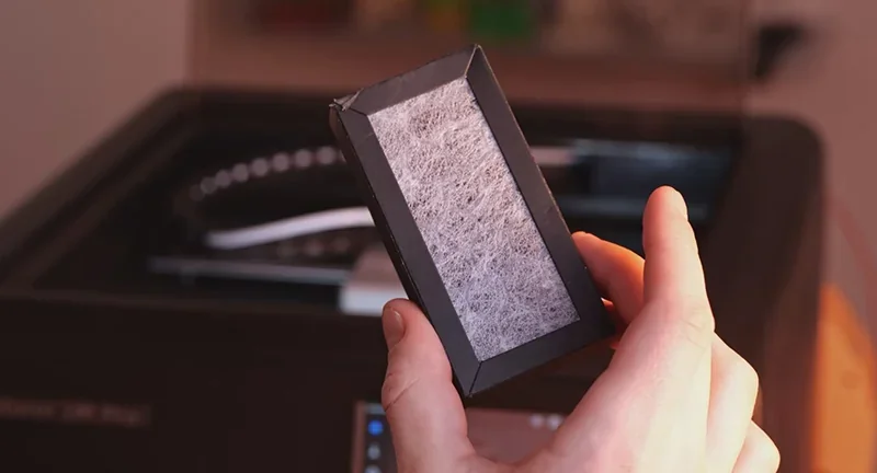 Flashforge Adventurer 5M Pro filter held by a hand, showcasing internal components and detailing work environment.