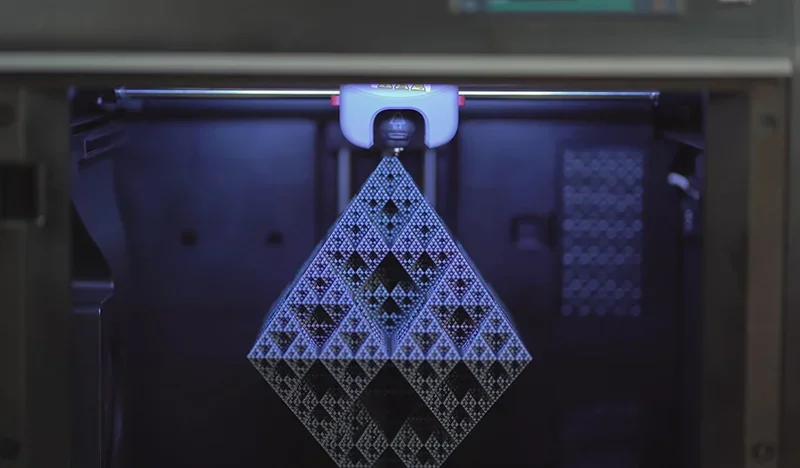Flashforge Adventurer 5M Pro 3D printer creating a detailed triangular structure under blue lighting, showing precision and intricate design capability.