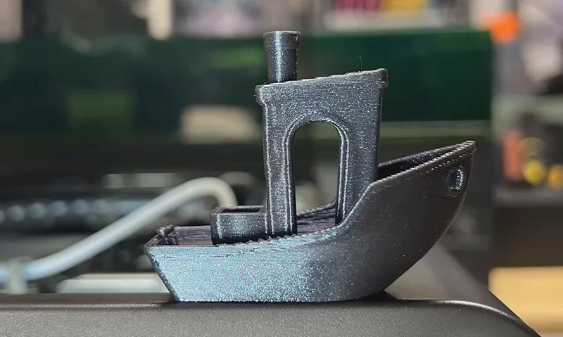 Flashforge Adventurer 5M Pro 3D-printed black boat model on printer, detailed design, set in a workshop environment.